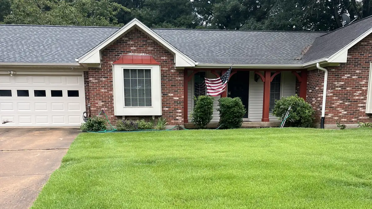 Finished front yard: a freshly mown lawn in front of a brick ranch house with a red-posted porch and a two-car garage